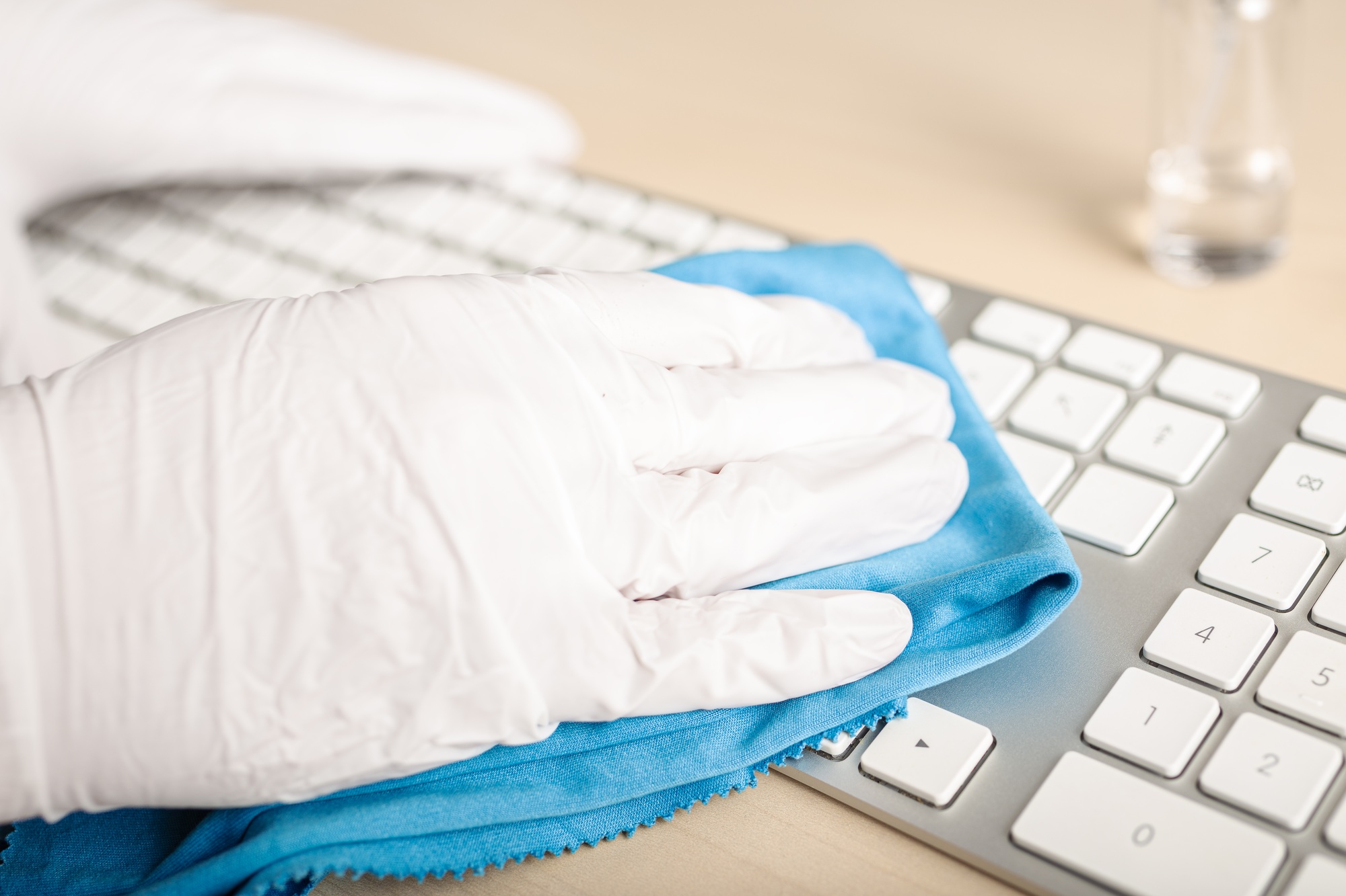 Hand with protective glove cleaning a keyboard with disinfectant